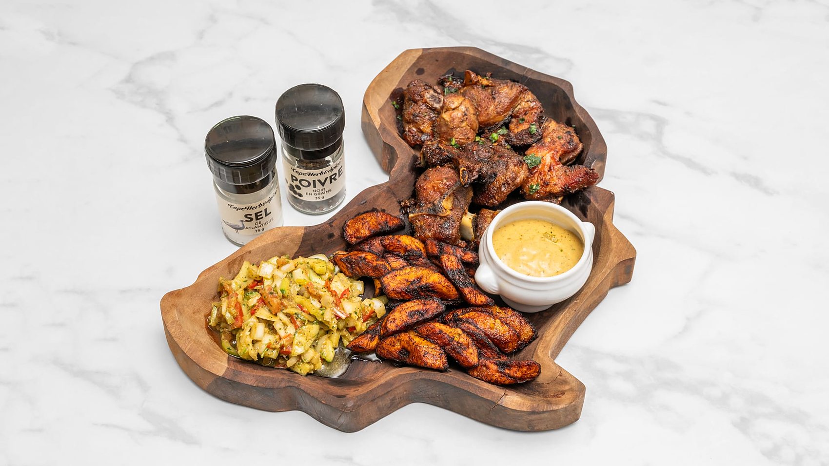 Dibi d'agneau grillé au charbon, aloko dorés et sauce moutarde sur une planche sculptée en forme d'Afrique